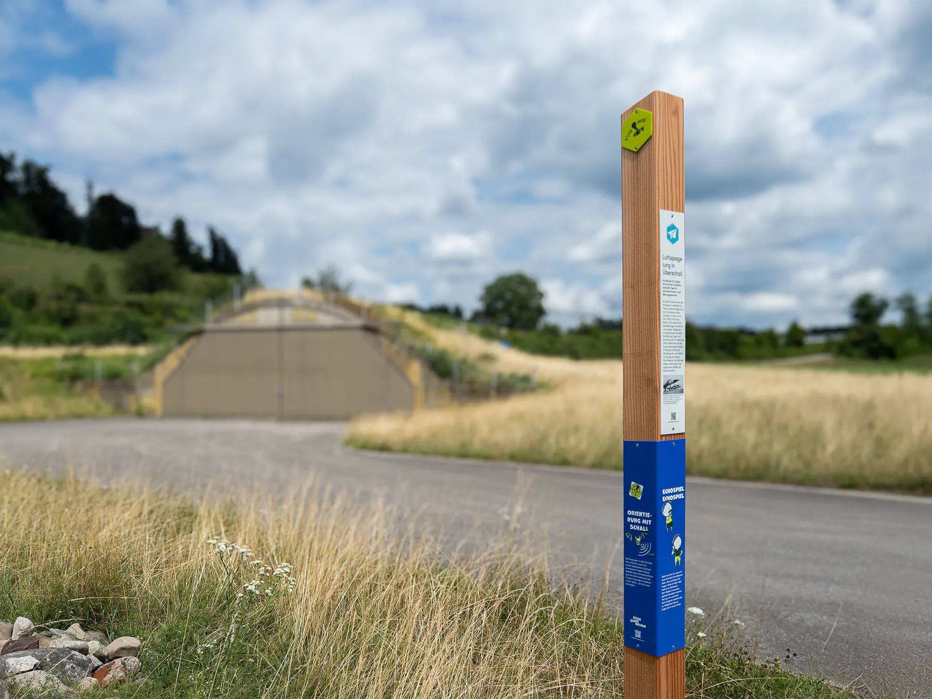 Balken mit Information, Zisch-Summ-Brumm-Abenteuerweg und Blick auf den Hangar ©Signito GmbH